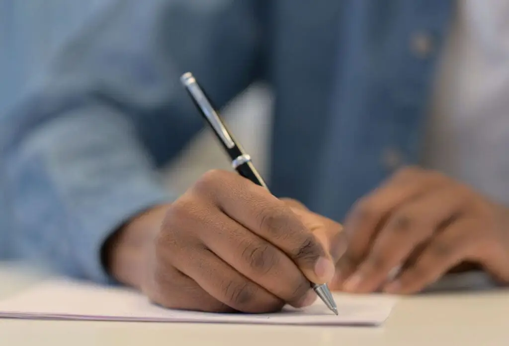 Hands of African Man Writing on Paper with Pen, Close Up
